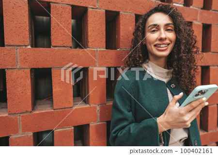 Beautiful young woman in green coat using her cellphone in the city 100402161