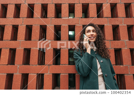 Young woman talking on mobile phone while walking in the city 100402354