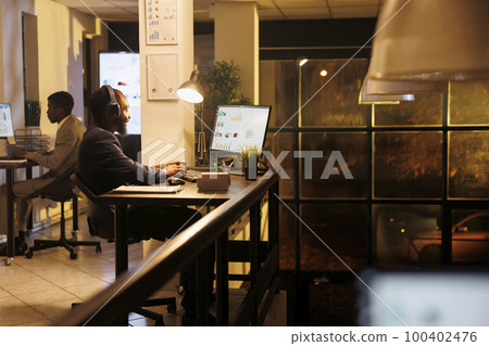 Executive manager with headpones listening music in startup office, analyzing financial graph report, planning investment strategy to help increase company proft. Employee working late at night Executive manager with headpones listening music in startup office, analyzing financial graph report, planning investment strategy to help increase company proft. Employee working late at night 100402476