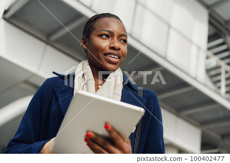 Smiling african woman holding digital tablet while walking outdoors. Smiling african woman holding digital tablet while walking outdoors. 100402477