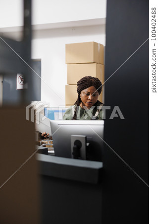 African american worker analyzing goods quality control report on computer, working at merchandise inventory in warehouse. Storage room employee preparing customers orders for delivery 100402488