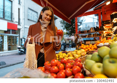 Good looking young woman standing in front of fruit shelves buying groceries in the street 100402491