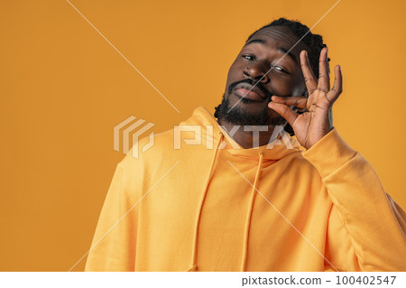African man standing over yellow background showing silence gesture 100402547