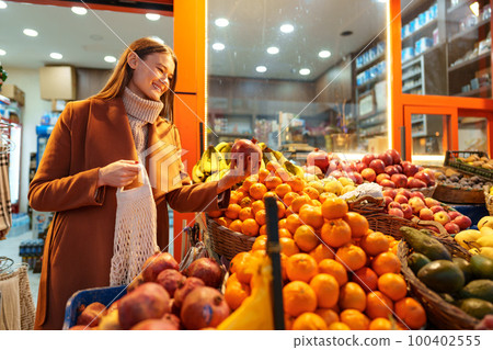 Good looking young woman standing in front of fruit shelves buying groceries in the street Good looking young woman standing in front of fruit shelves buying groceries in the street 100402555