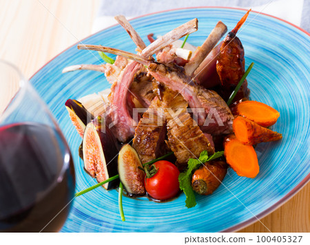 Baked tasty lamb ribs served with carrots, tomatoes and fresh figs 100405327