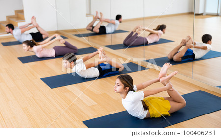 Teen girl doing asana Dhanurasana during family yoga workout at gym Teen girl doing asana Dhanurasana during family yoga workout at gym 100406231