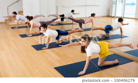 Preteen girl doing Dandayamna Bharmanasana during yoga training with family 100406279