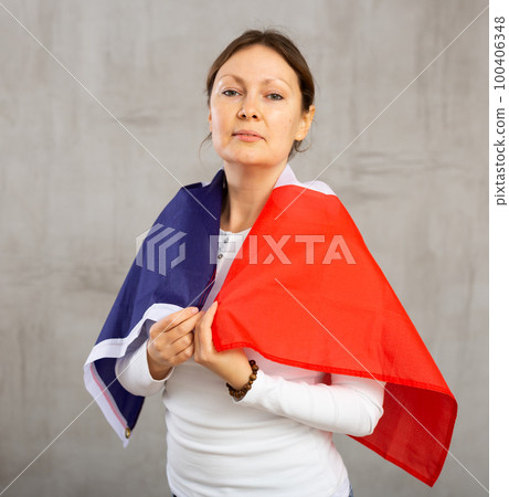 Calm female with serious expression on face standing against gray wall with national flag of France 100406348