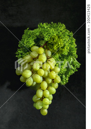 A bunch of ripe grapes with green lettuce leaves on a dark background 100413426