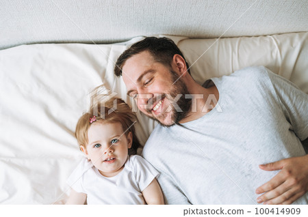 Young happy family with father and daughter baby girl on bed in cozy home, view from top Young happy family with father and daughter baby girl on bed in cozy home, view from top 100414909