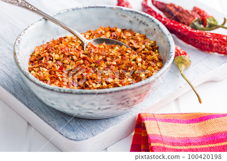 Dry chili pepper flakes. Crushed red peppers in bowl on white table. 100420198