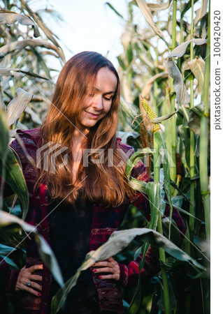 Brown-haired woman looks exploring leaf on corn field 100420420