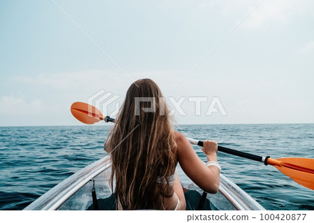Woman in kayak back view. Happy young woman with long hair floating in transparent kayak on the crystal clear sea. Summer holiday vacation and cheerful female people relaxing having fun on the boat Woman in kayak back view. Happy young woman with long hair floating in transparent kayak on the crystal clear sea. Summer holiday vacation and cheerful female people relaxing having fun on the boat 100420877