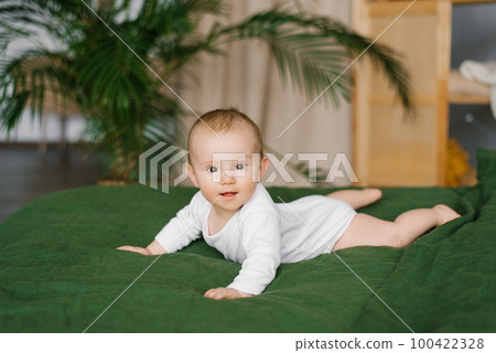 Small beautiful child lies on the bed on his stomach and smiles. happy toddler boy on green bedspread at home 100422328