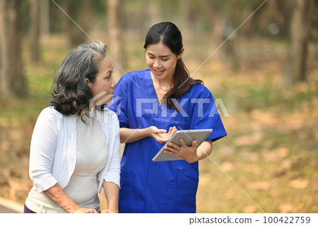 Female doctor in uniform holding digital tablet explaining therapy details to elderly patient. Assistance and rehabilitation 100422759