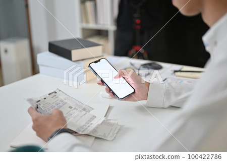 Man using mobile smart phone for paying electricity bills at desk. Internet banking and expenses concept 100422786
