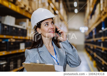Manager woman in suit calling in a waehouse. 100424318