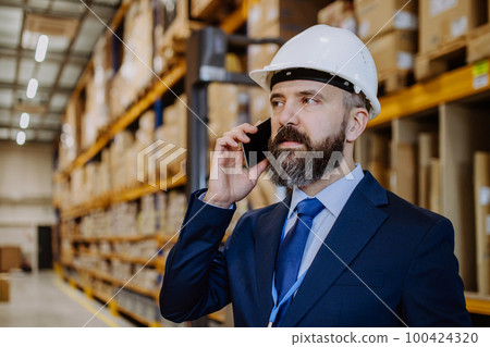 Manager woman in suit calling in a waehouse. 100424320