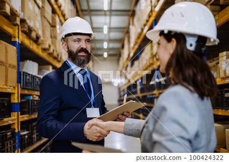 Managers in suits shaking hands in warehouse. 100424322