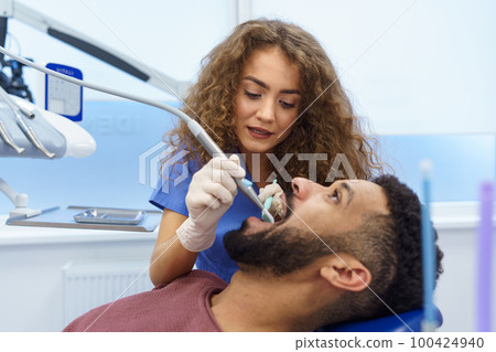 Young woman dentist doing preventive examination to multiracial man. 100424940