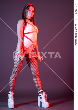 Beautiful young gogo dancer woman posing in front of a background dressed in a pinup style. Beautiful young gogo dancer woman posing in front of a background dressed in a pinup style. 100426126