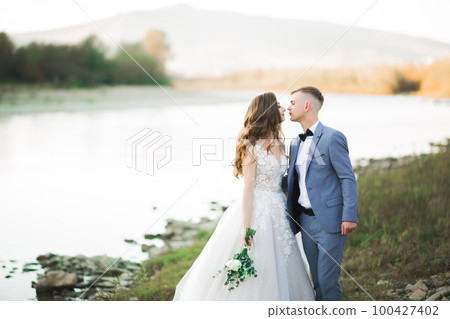 Elegant stylish happy blonde bride and gorgeous groom on the background of a beautiful river in the mountains 100427402
