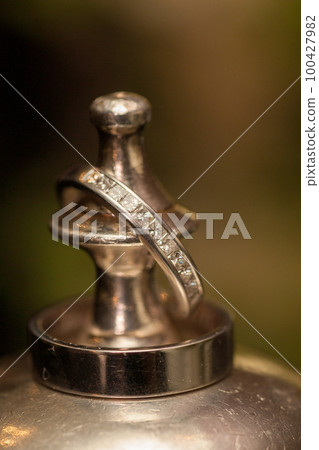 wedding rings detail on metal chalice with bridal bouquet in the background, bride and groom wedding wedding rings detail on metal chalice with bridal bouquet in the background, bride and groom wedding 100427982