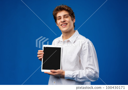 Happy young man showing digital tablet isolated on blue background. 100430171