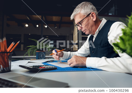 Mature man working on architectural project in office Mature man working on architectural project in office 100430296