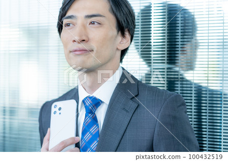 Portrait of businessman standing in office building with smartphone in hand 100432519