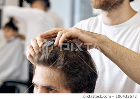 close-up, professional male hairstylist combing young customer's hair 100432678