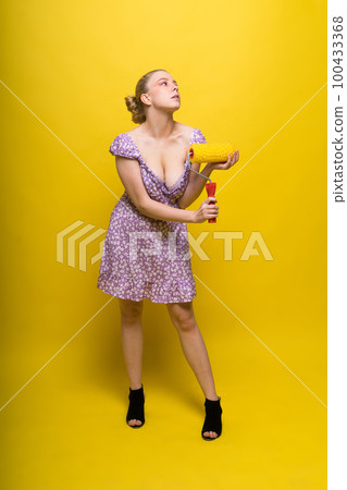 Young classic pin-up woman painting wall with paint roller 100433368