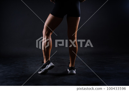 Shaped female legs in sneakers sculpted in muscles, dark background 100433596