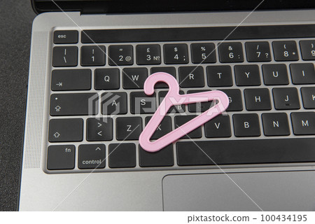 Small pink hanger for clothes on laptop keyboard. Online shopping, buying clothes on the Internet. Online clothing store 100434195