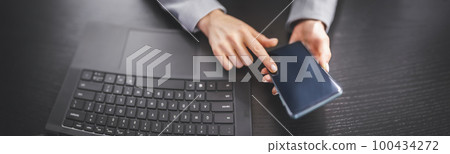 Woman holding in her hands mobile phone and typing on the laptop. 100434272