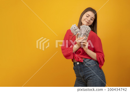 Teenage girl holds wad of U.S. dollars and smiles. Successful youth. Young business woman. Rich and carefree concept. Copy space. Teenage girl holds wad of U.S. dollars and smiles. Successful youth. Young business woman. Rich and carefree concept. Copy space. 100434742