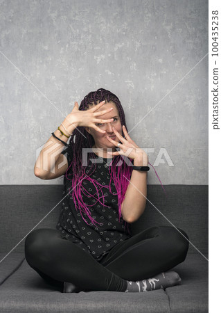 Funny young woman with dreadlocks sits on the couch and actively gesticulates. Freaky girl. Vertical frame. Funny young woman with dreadlocks sits on the couch and actively gesticulates. Freaky girl. Vertical frame. 100435238