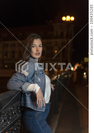 Attractive stylish girl on night city street. Portrait of young woman in denim jacket on evening city background Attractive stylish girl on night city street. Portrait of young woman in denim jacket on evening city background 100435285