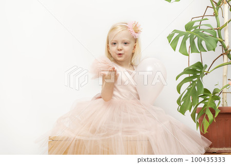 Smiling Blond little girl with balloon. Little girl in pink dress and crown hoop on head.Monstera flower on background 100435333