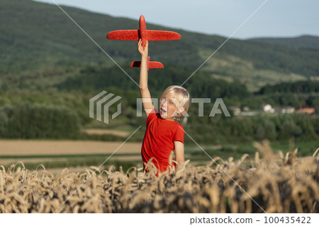 Happy boy in red T-shirt plays with toy plane in wheat field on mountains background. Flights and travel with children. Happy boy in red T-shirt plays with toy plane in wheat field on mountains background. Flights and travel with children. 100435422