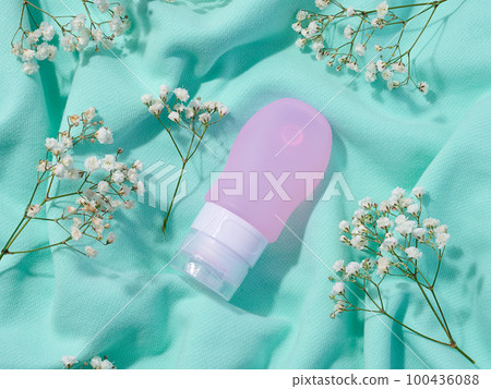 Pink plastic tube for cosmetics and sprigs of white gypsophila flowers, top view 100436088