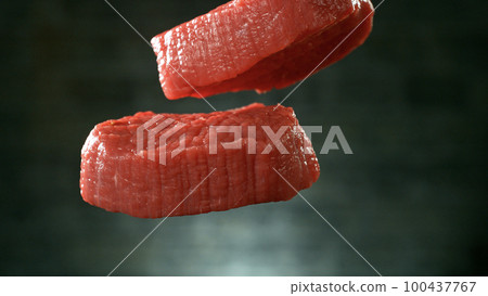 Flying pieces of raw beef steaks falling on table, grey brick wall on background. Flying pieces of raw beef steaks falling on table, grey brick wall on background. 100437767