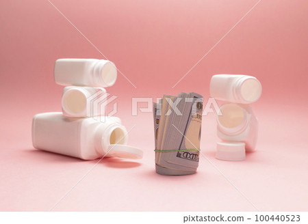 American dollars in roll, empty pills, vitamin bottles, containers on pink background. Medical, pharmaceutical business. Price, consumption concept. Medical expenses. Horizontal plane, copy space. American dollars in roll, empty pills, vitamin bottles, containers on pink background. Medical, pharmaceutical business. Price, consumption concept. Medical expenses. Horizontal plane, copy space. 100440523