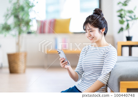 A young woman using a smartphone in the living room. A young woman using a smartphone in the living room. 100440748
