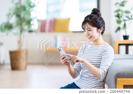 A young woman using a smartphone in the living room. A young woman using a smartphone in the living room. 100440749