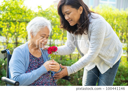 Caregver help Asian elderly woman holding red rose flower, smile and happy in the sunny garden. 100441146