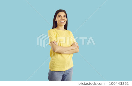 Happy woman in yellow T shirt standing with her arms crossed isolated on blue background 100443261