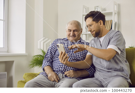 Young brunette nurse man helping a senior patient how to use smartphone. 100443270