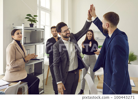 Two male colleagues doing high five at meeting in office 100443271