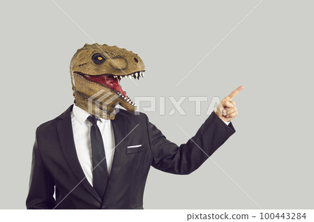 Strange businessman in suit and funny dinosaur monster mask pointing to the side 100443284
